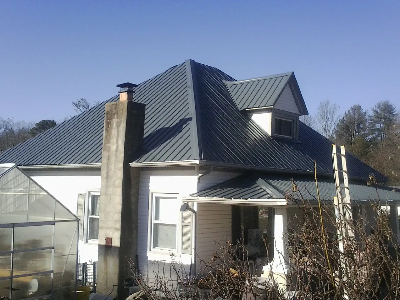 Dark blue standing seam metal roof on a white farmhouse with dormer — Slate & Tile Roof Repair by Roofing Brothers in New Columbia