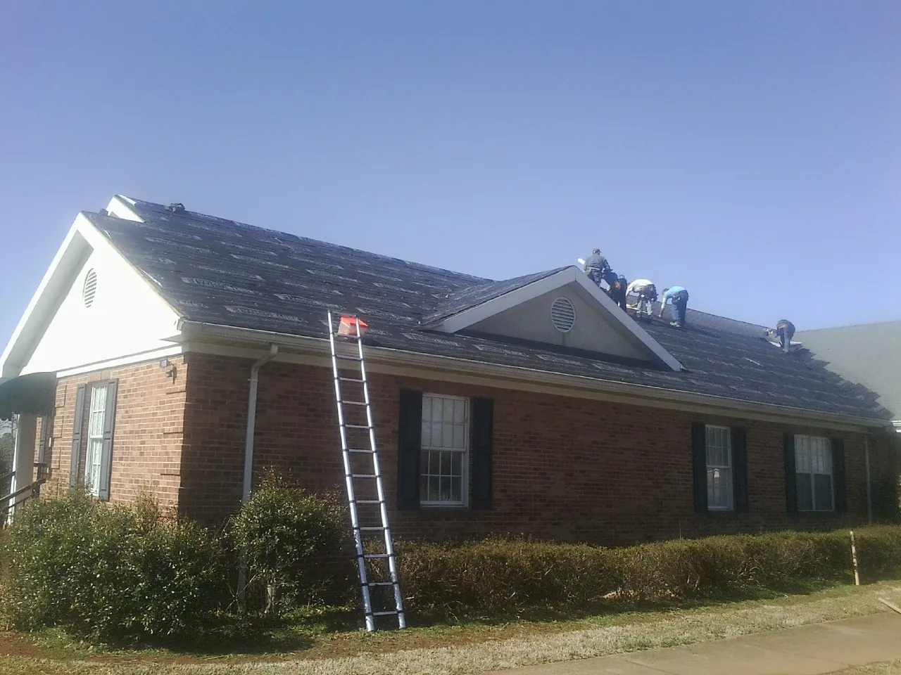Crew tearing shingles off a brick ranch roof with a ladder set — Metal Roof Repair work by our crew in New Columbia