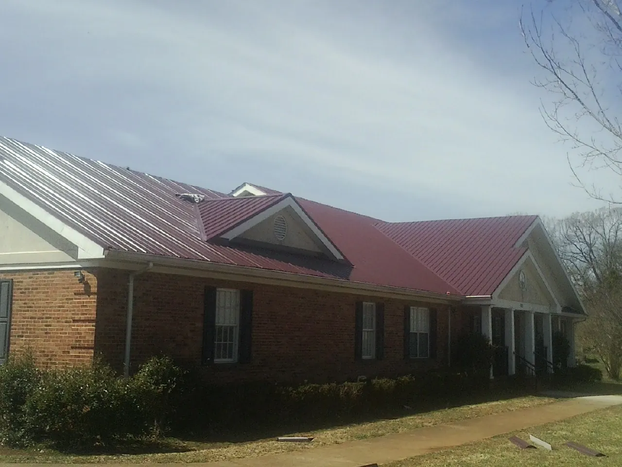 Red metal roof with gabled entries on a long brick building, from a Hail Damage Roof Repair job in New Columbia