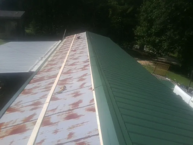 Old rusted panels beside newly installed green metal roofing — Wind Damage Roof Repair by Roofing Brothers in New Columbia