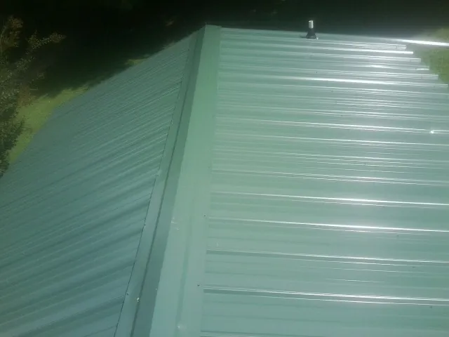New green metal panels meeting at the ridge of a roof — Flat Roof Repair work by our crew in New Columbia