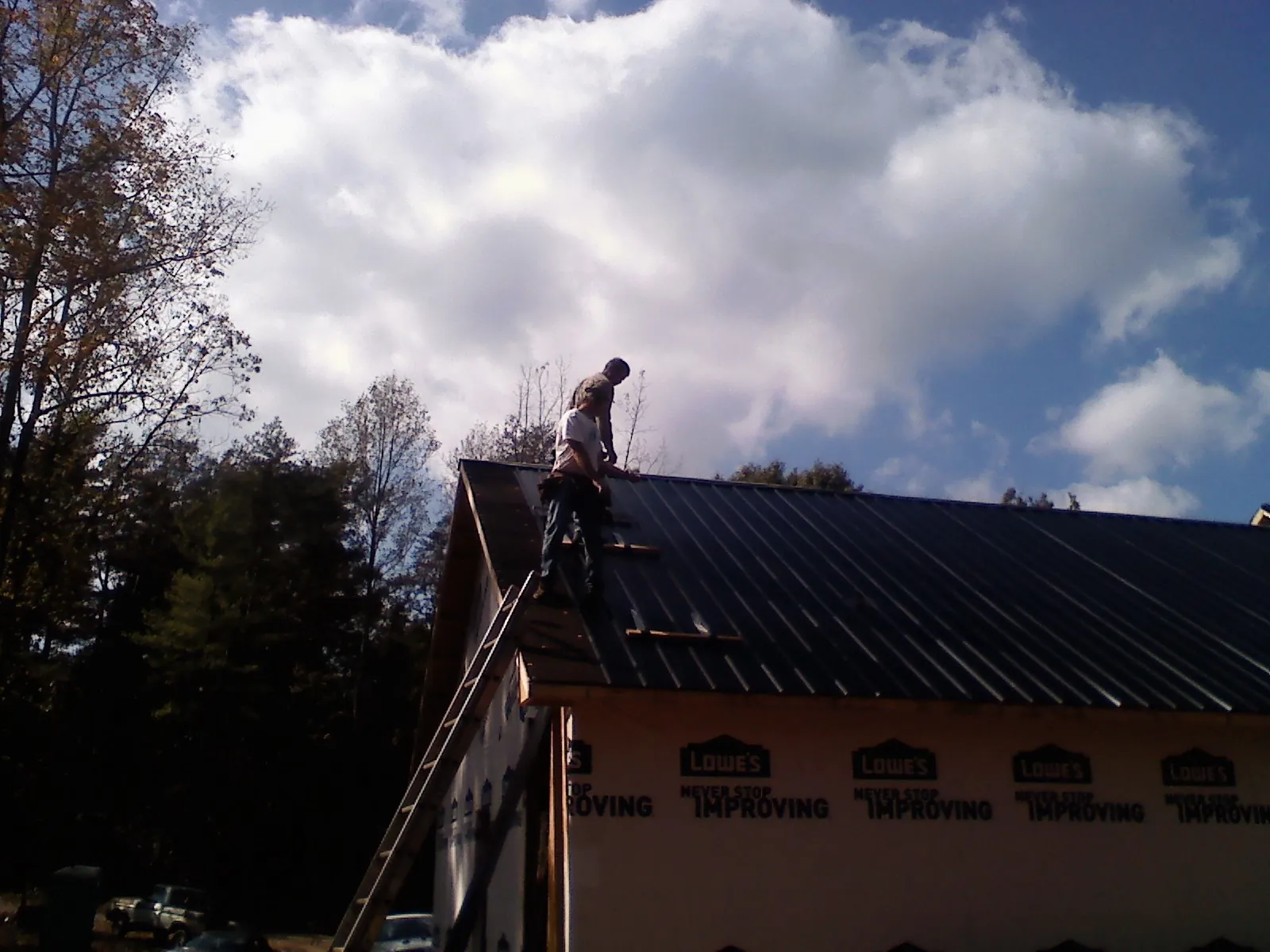 Roofer fastening dark metal panels high against a cloudy sky, from a Roof Inspection job in New Columbia