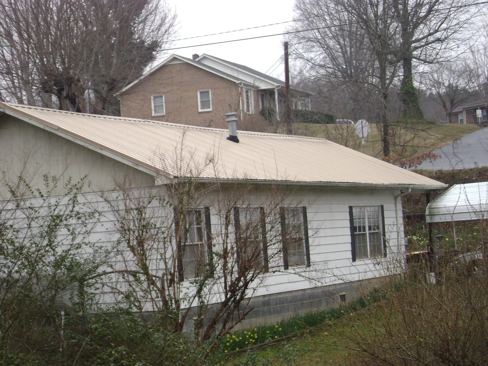 Tan metal roof on a white sided house set into a hillside — Commercial Roofing by Roofing Brothers in New Columbia